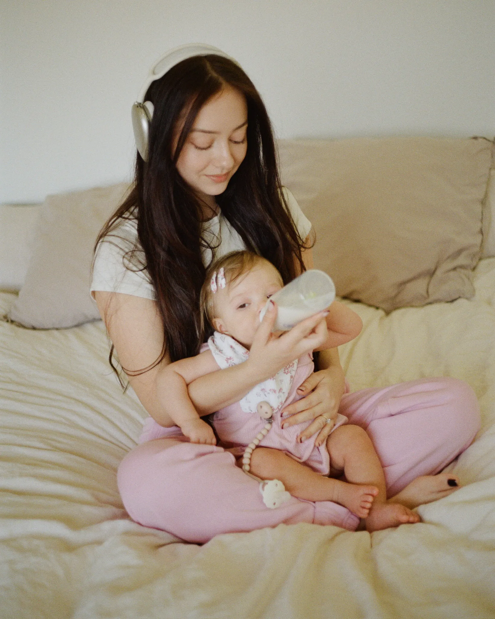 A mother feeding her baby on the bed with her headphones on.